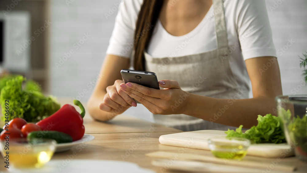 Woman choosing salad recipe on smartphone at the kitchen, cooking application