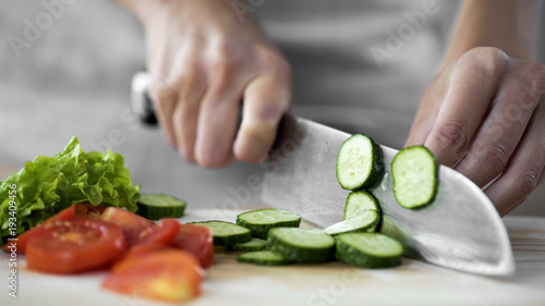 Fotografie Housewife hands cutting cucumber on kitchen board, vegetable salad cooking steps