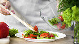 Female pouring salad appetizer on dinner plate from bowl, weight loss, dieting