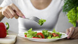 Housewife taking green lettuce salad from white plate in kitchen, fresh food
