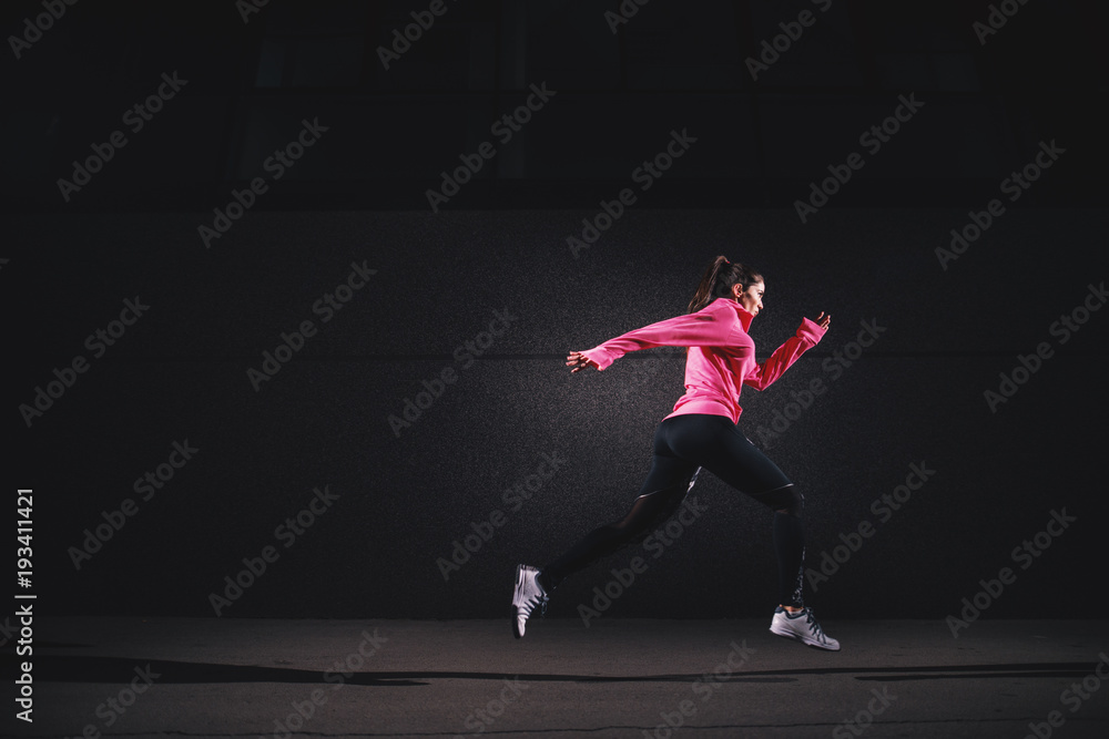 Side motion view of sexy fit athlete running girl in sportswear at the street in front of the grey wall.