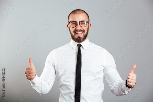 Image of ecstatic caucasian man in white shirt and eyeglasses smiling and showing thumbs up, isolated over gray background