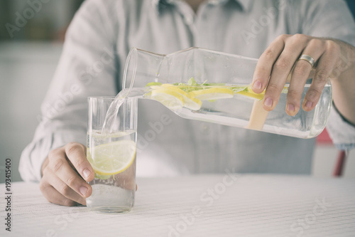 Young man pouring water from bottle to water in kitchen