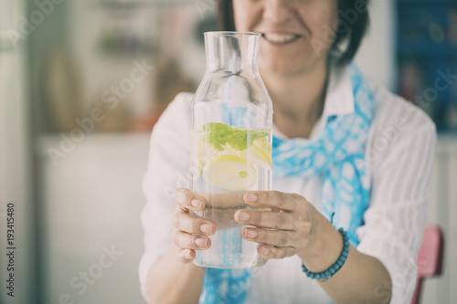 Woman holding  bottle with water lemon and mint in kitchen