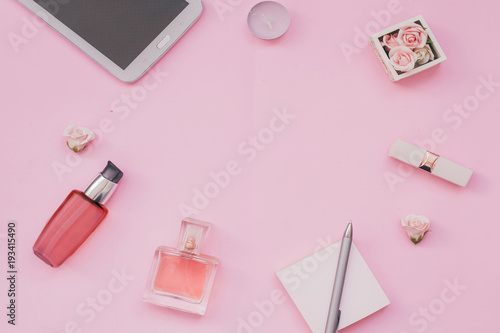Pink background with female accessories perfume, cream, lipstick, laptop