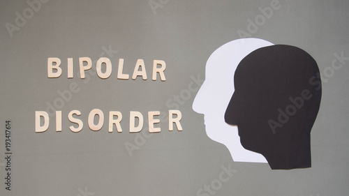 Bipolar disorder presented by double human head made from black and white paper on gray background w/ wood word. Manic and depress emotion. Mental health, brain disorder and psychological concept. photo