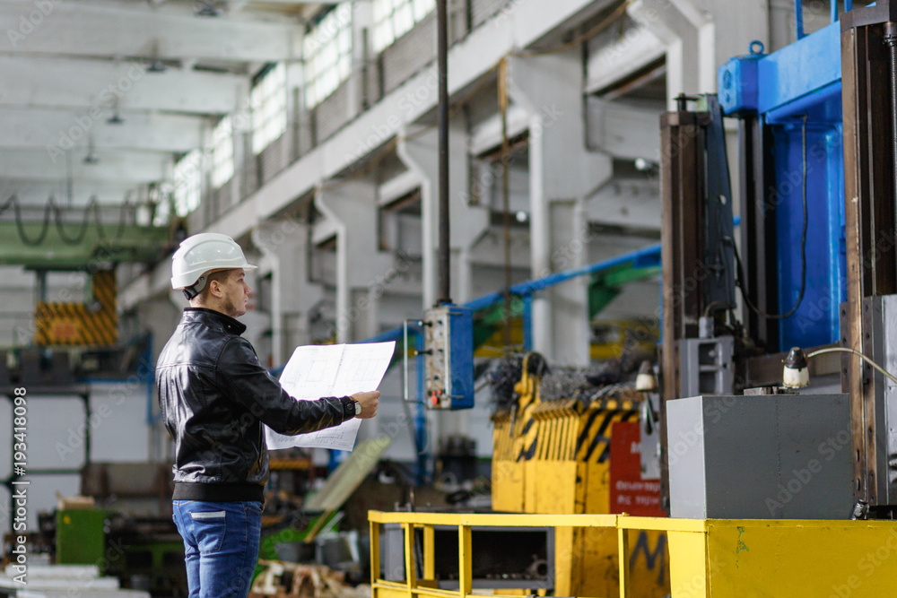 A young successful engineer with a drawing in his hands is standing in the territory of a modern factory. A young successful engineer with a drawing in his hands is standing in the territory of a modern factory.