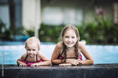 Funny little kids girls smile and swim in the outdoor swimming pool beautiful and happy