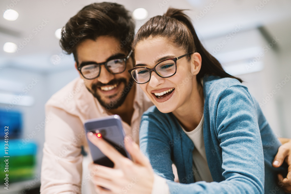 Two beautiful happy young people checking out the mobile specifications while shopping in the electronic store. Two beautiful happy young people checking out the mobile specifications while shopping in the electronic store.