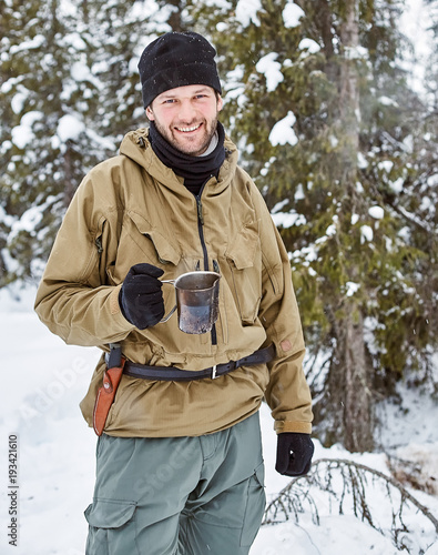 Young smiling man in outdoors clothes with metal mug in his hand