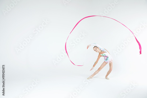 Rhythmic gymnastics caucasian blonde girl in dress for show performing athlete exercises with pink ribbon handling abilities showing flexibility and acrobat balance on white background isolated