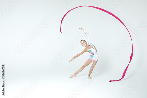 Rhythmic gymnastics caucasian blonde girl in dress for show performing athlete exercises with pink ribbon handling abilities showing flexibility and acrobat balance on white background isolated