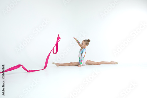 Rhythmic gymnastics caucasian blonde girl in dress for show performing athlete exercises with pink ribbon handling abilities showing flexibility and acrobat balance on white background isolated