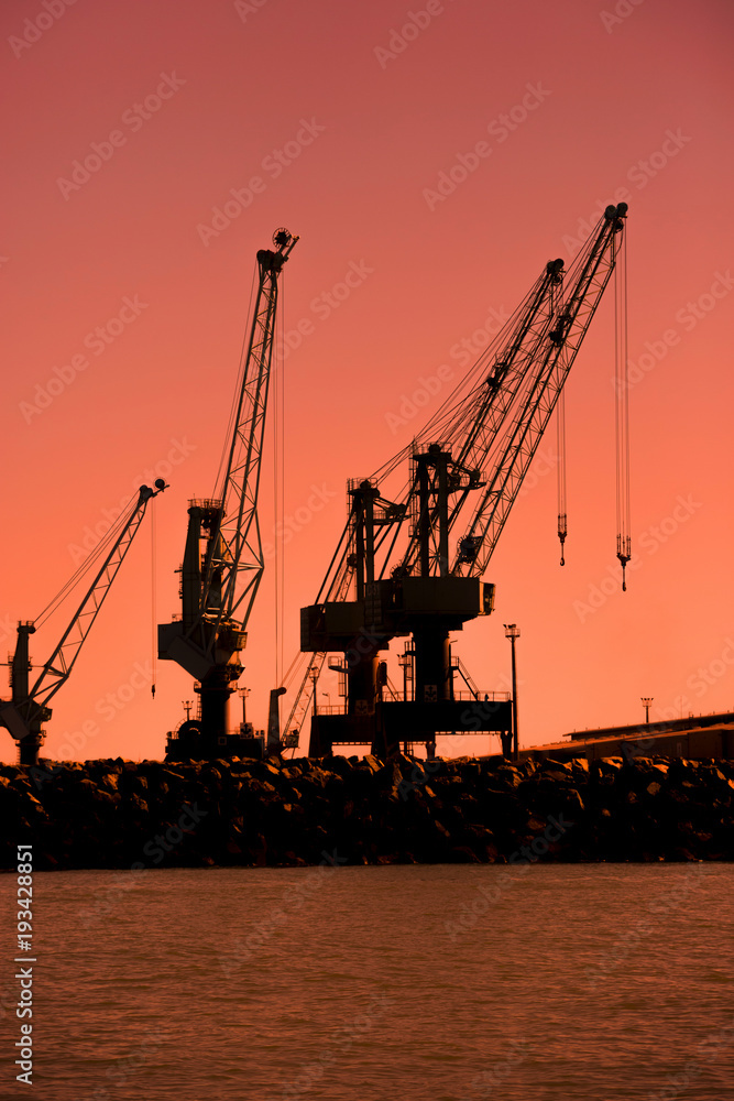 Shipyard cranes silhouetted against a beautiful orange sunset.