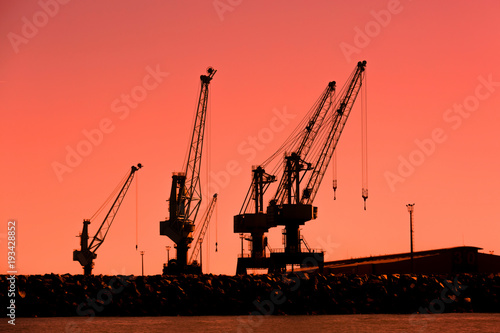 Shipyard cranes silhouetted against a beautiful orange sunset.