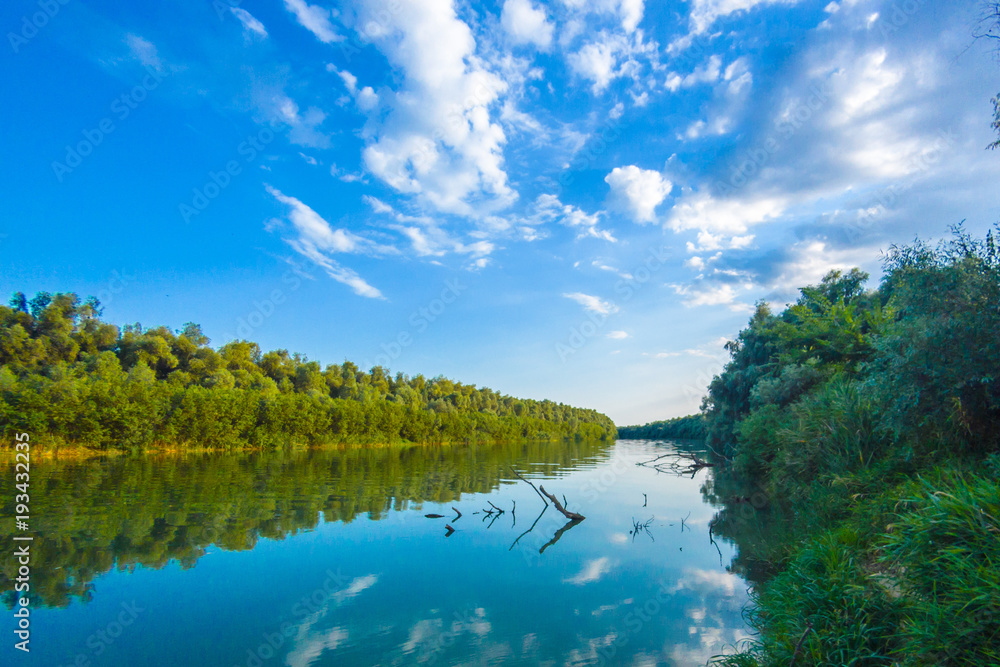 Riverbank of calm Danube river with green trees in spring or summer and deep blue sky with clouds at the setting sun. Ukraine Riverbank of calm Danube river with green trees in spring or summer and deep blue sky with clouds at the setting sun. Ukraine