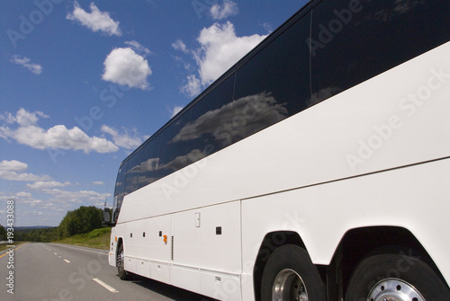 clean side view of tour bus on highway with clouds and blue sky