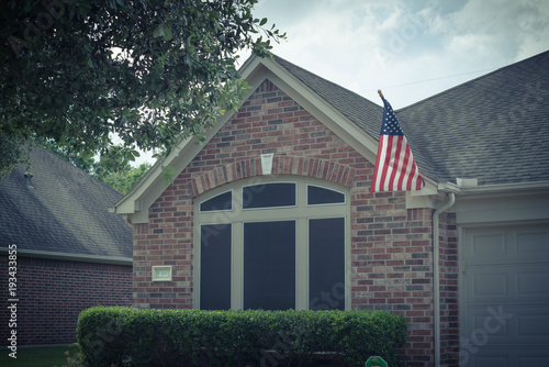 Front porch of typical one story house proudly displaying American flag. Vintage tone