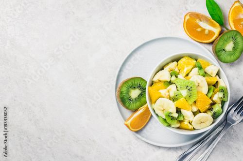 Citrus, kiwi, banana fruit salad on white background. Top view, copy space.