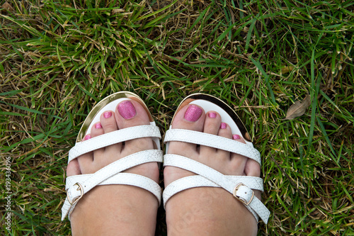White sandals on female feet with nail Polish on the background of green grass in the summer