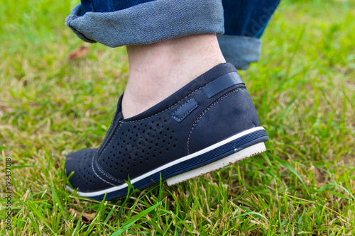 A man in jeans and summer shoes on the background of green grass . Loafers.