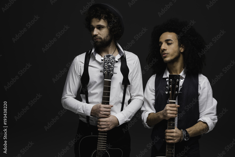 Obraz premium duet of handsome young musicians with acoustic guitars looking away on black