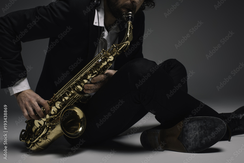 Naklejka premium cropped shot of musician playing saxophone while sitting on floor