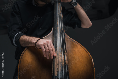 cropped shot of man playing contrabass on black photo