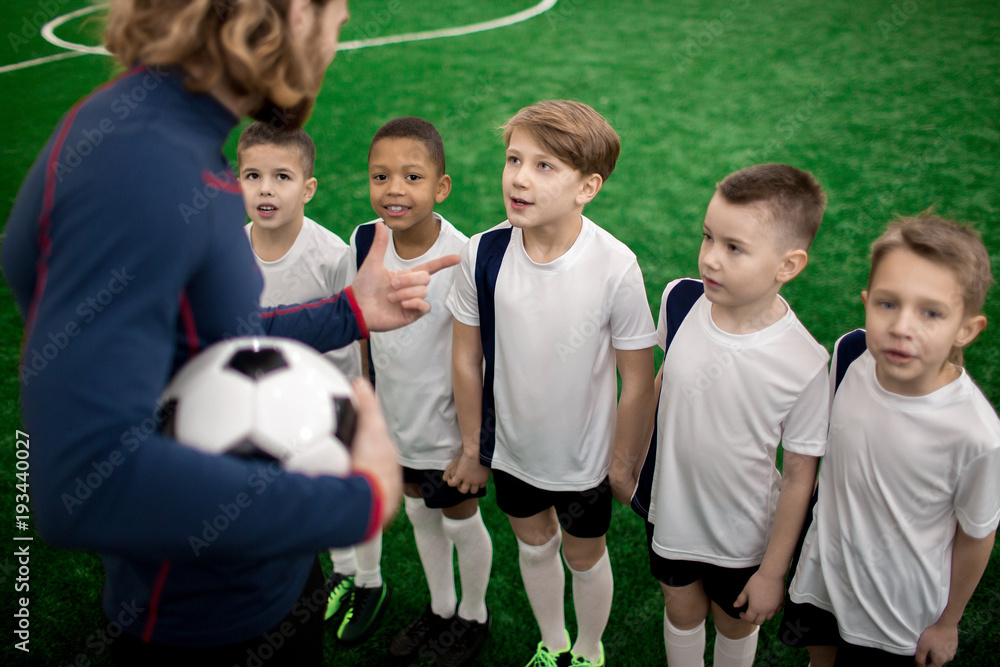 One of boys talking to football trainer between games among his groupmates One of boys talking to football trainer between games among his groupmates