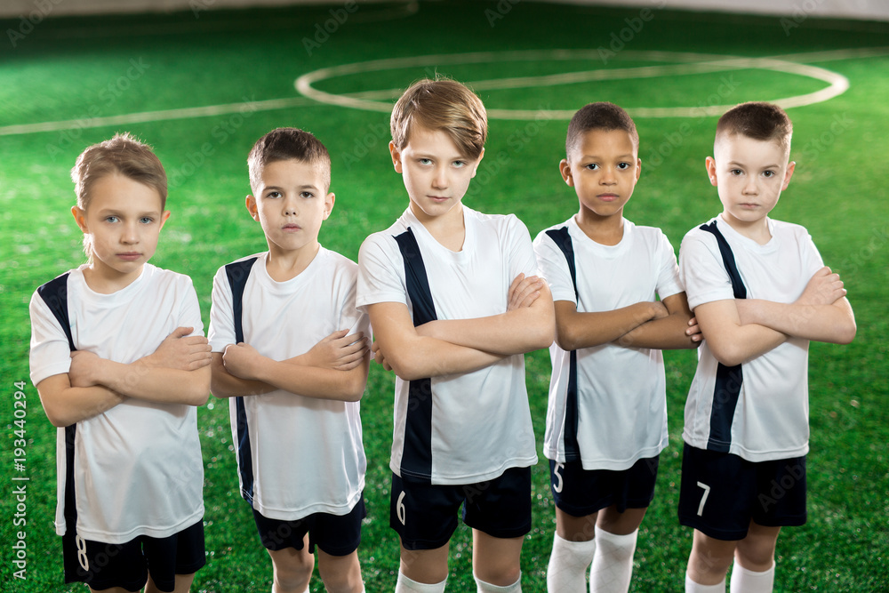 Row of little confident soccer players in uniform with arms crossed on chest looking at camera