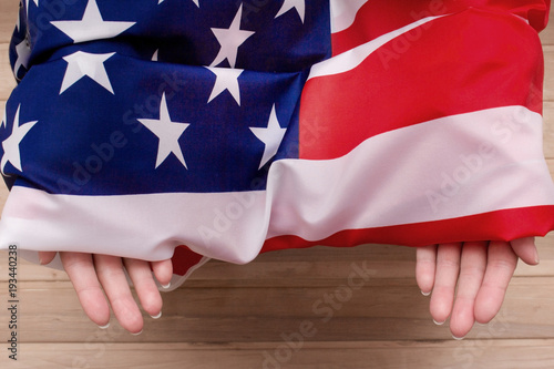 Fototapeta Naklejka Na Ścianę i Meble -  The American flag holds in his hands on a light wooden background. The Flag Of The United States Of America.