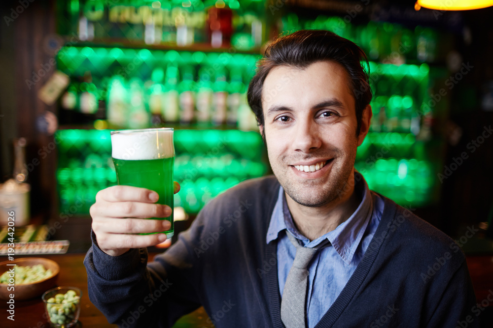 Young man with toothy smile holding glass of foaming beer while spending time in pub Young man with toothy smile holding glass of foaming beer while spending time in pub