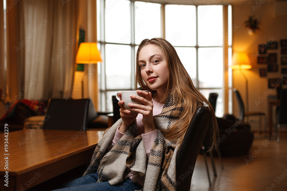 Gorgeous happy woman drinks coffee at a cafe background. Covered cozy plaid. Blurred cafe background. Gorgeous happy woman drinks coffee at a cafe background. Covered cozy plaid. Blurred cafe background.