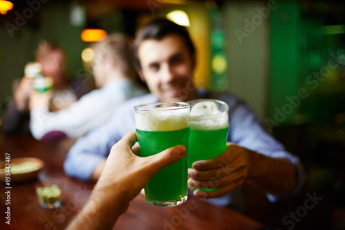 Male hands clinking by glasses of green foaming beer over bar counter in pub