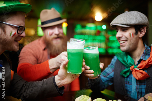 Happy irish football fans clinking with glasses of green foaming beer in pub