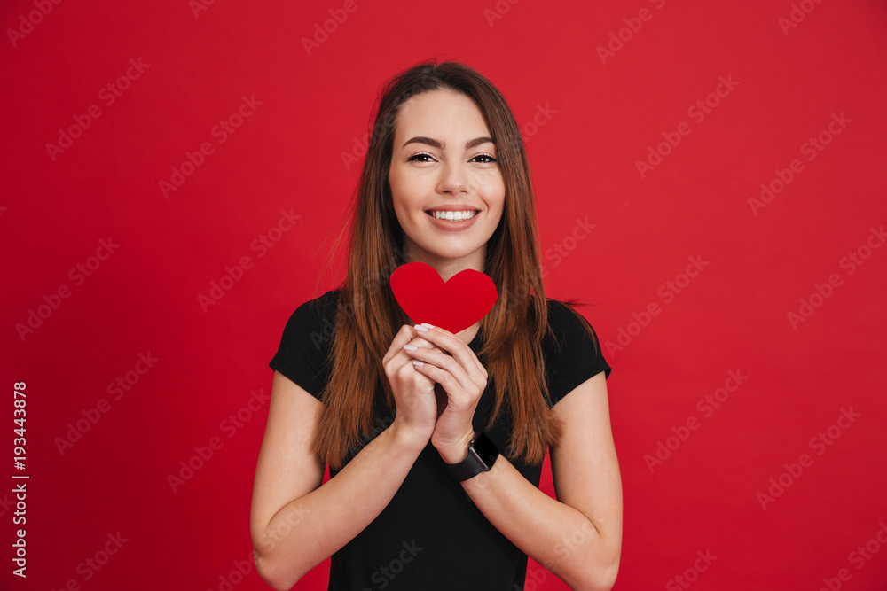 Romantic adorable woman 20s with long brown hair holding paper heart in valentine day, isolated over red background Romantic adorable woman 20s with long brown hair holding paper heart in valentine day, isolated over red background