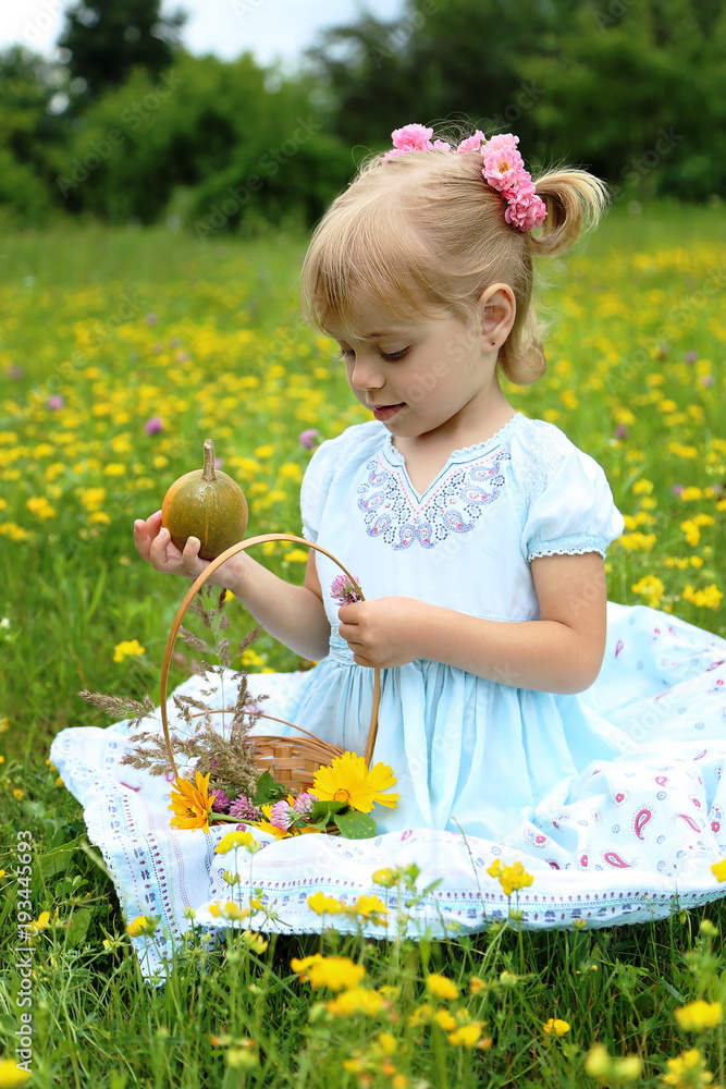 A little blonde caucasian child girl in light blue dress and roses