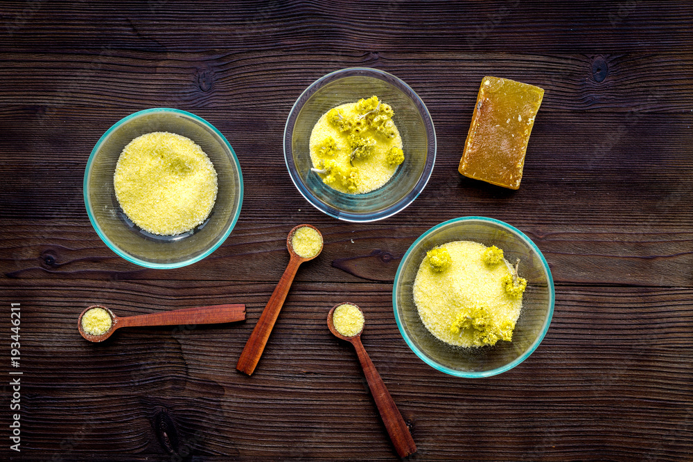Aromatic spa salt. Yellow spa salt with delicate spring flowers on dark wooden background top view Aromatic spa salt. Yellow spa salt with delicate spring flowers on dark wooden background top view