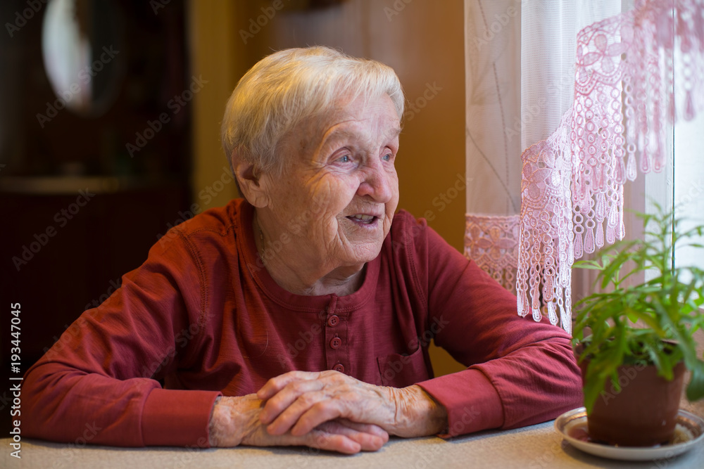 An elderly woman looks out the window sitting at the table. An elderly woman looks out the window sitting at the table.