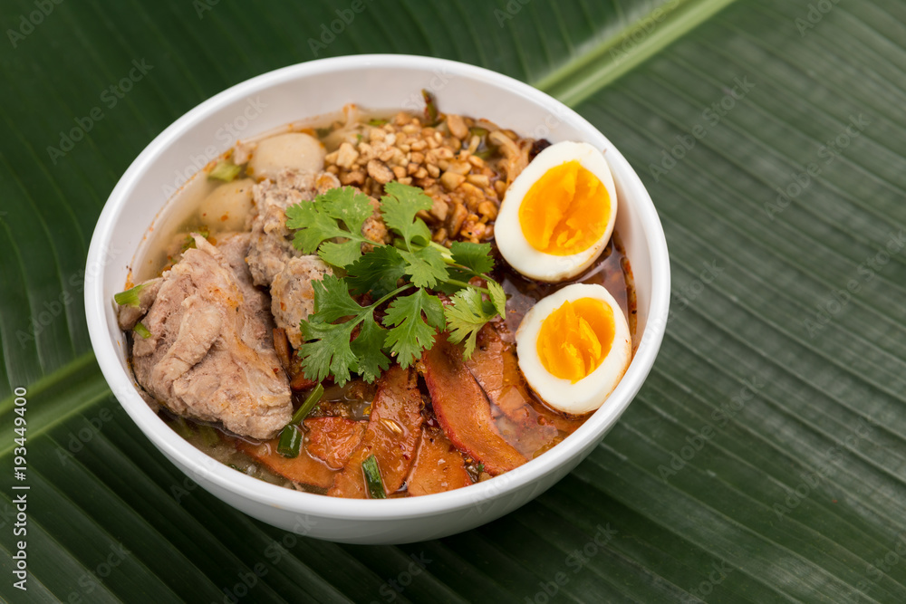 Spicy noodle soup with pork and egg in bowl on banana leaf Spicy noodle soup with pork and egg in bowl on banana leaf