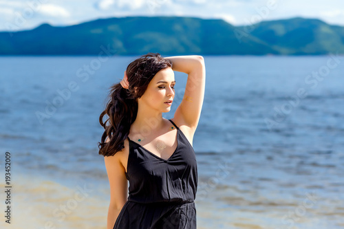 young beautiful girl stands on the background of water and mountains