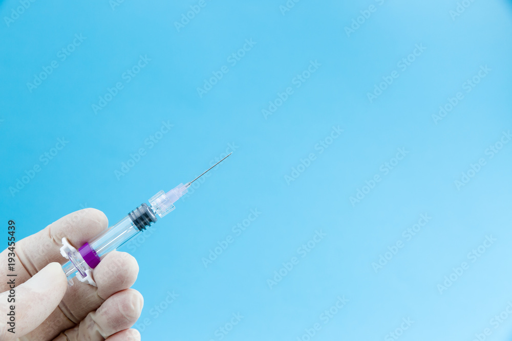 Syringe needle with influenza vaccine or medicine in doctors hands in white medical gloves isolated on blue background copy space Syringe needle with influenza vaccine or medicine in doctors hands in white medical gloves isolated on blue background copy space