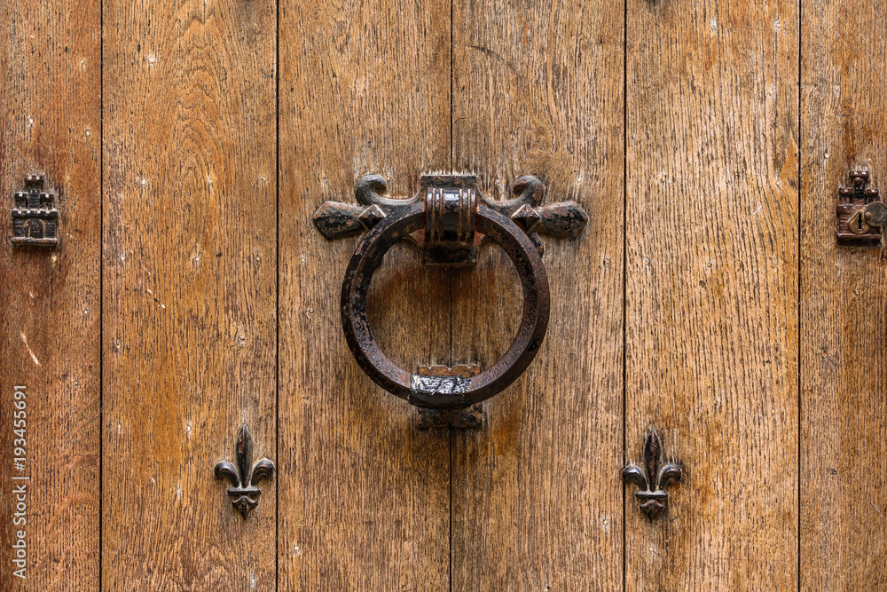 Ancient wooden entrance door with handle and fleur-de-lis ironwork. Saint-Denis, France Ancient wooden entrance door with handle and fleur-de-lis ironwork. Saint-Denis, France