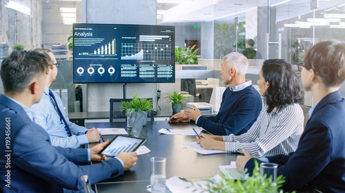 Obraz na plátně Diverse Group of Successful Business People in the Conference Room, Discuss  Company's Growth Shown on the Wall TV Illustrated by Charts and Statistics