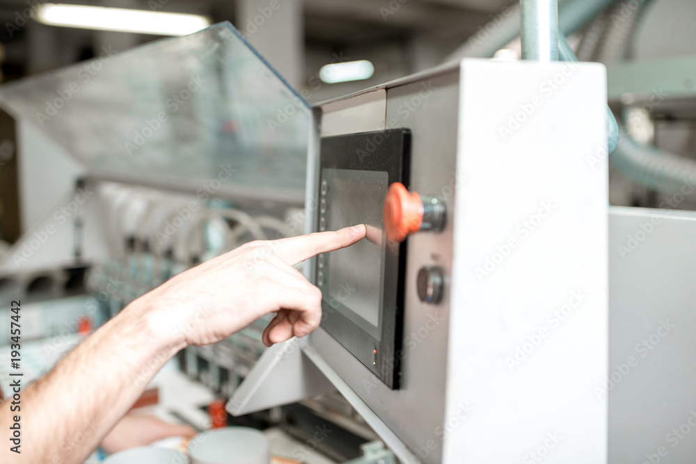 Obraz premium Pushing the button of the gluing machine which clings the label on the paper tube