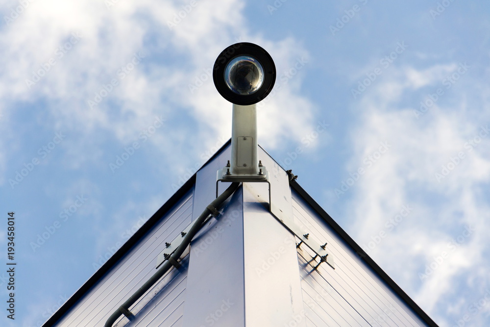 Modern dome security camera attached to wall with blue clear sky background copy space low angle view