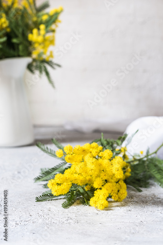 piccolo mazzo di mimosa in primo piano e vaso con altri fiori sfocato sullo sfondo