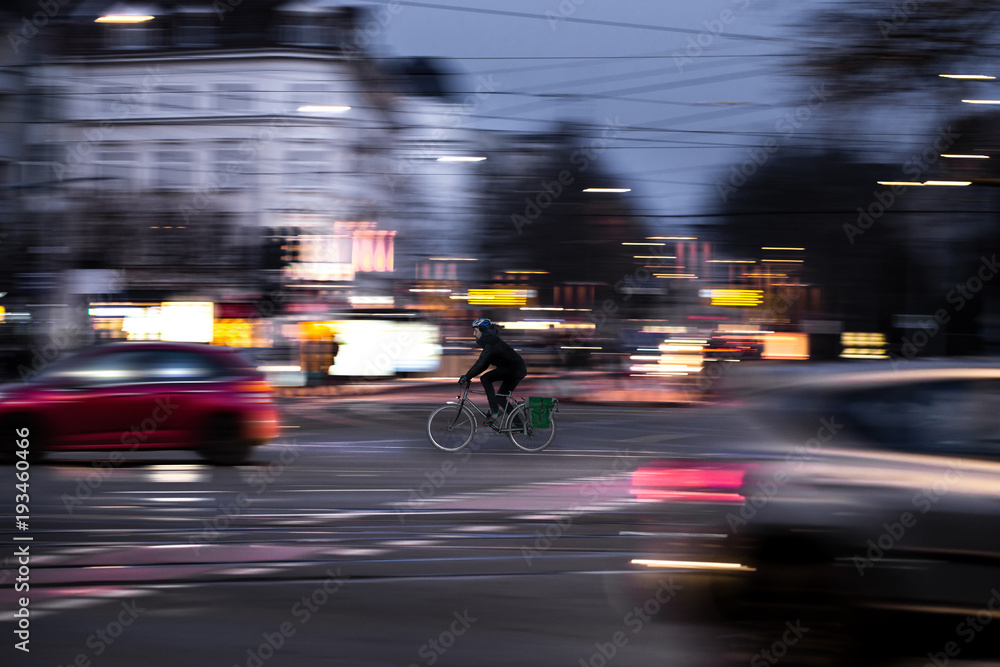 A cyclist drives at twilight over a road intersection - obrazy, fototapety, plakaty 