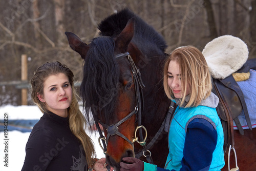 Two girls with white hair communicate with their horse. The girls finished riding a horse. A cloudy winter day. Close-up.