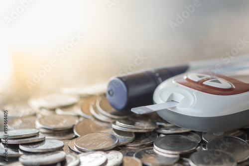 Close up of Glucose meter with lancet for check blood sugar level on pile of coins using as Medicine, diabetes, glycemia, health care and money concept. photo